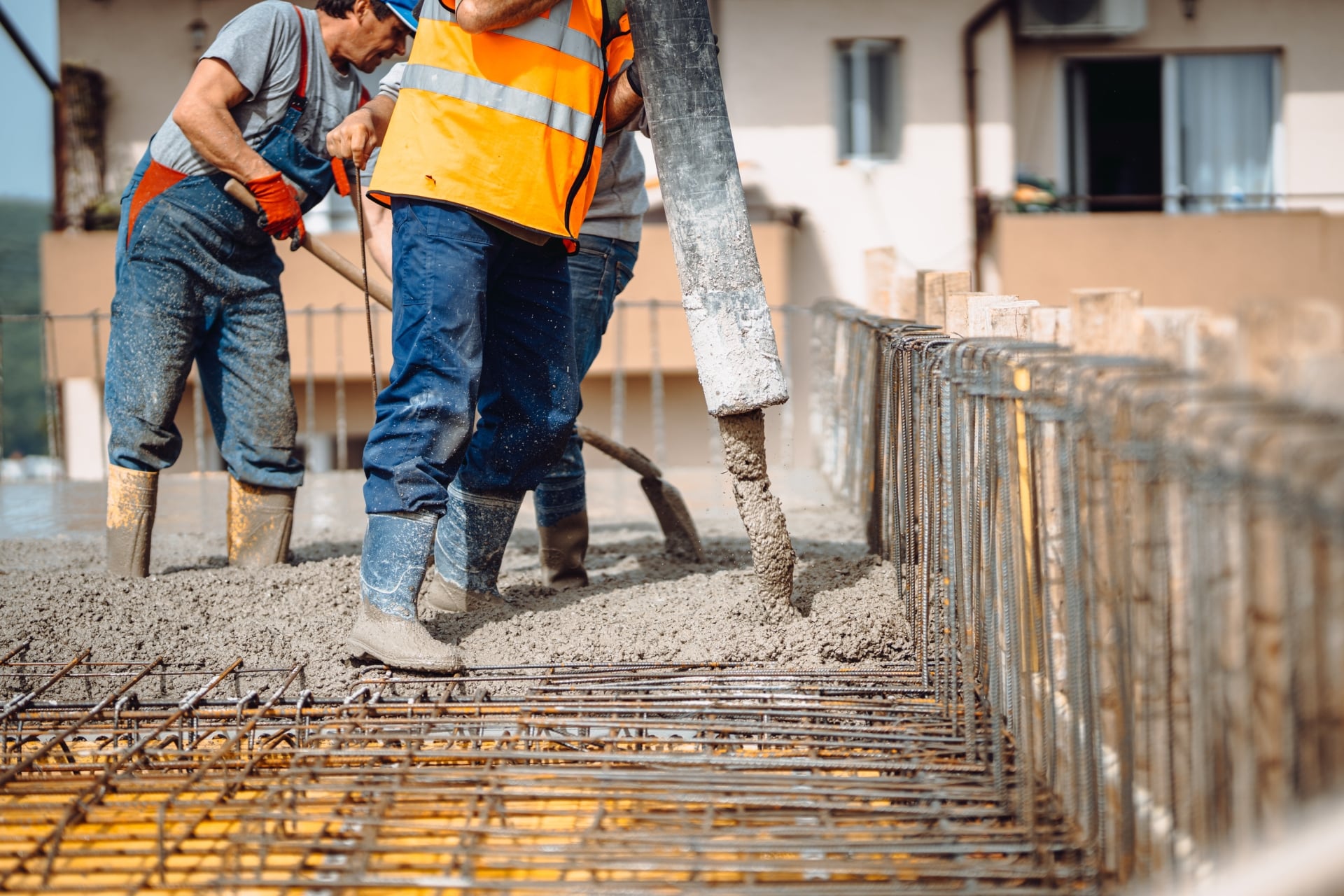 Team of workers pouring cement or concrete at construction site and using automatic pump