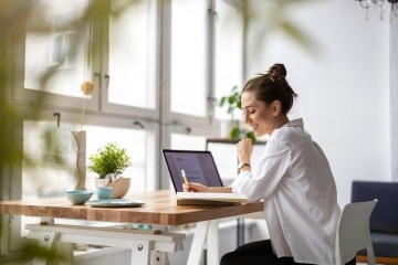 Woman writing on notebook with a laptop in front