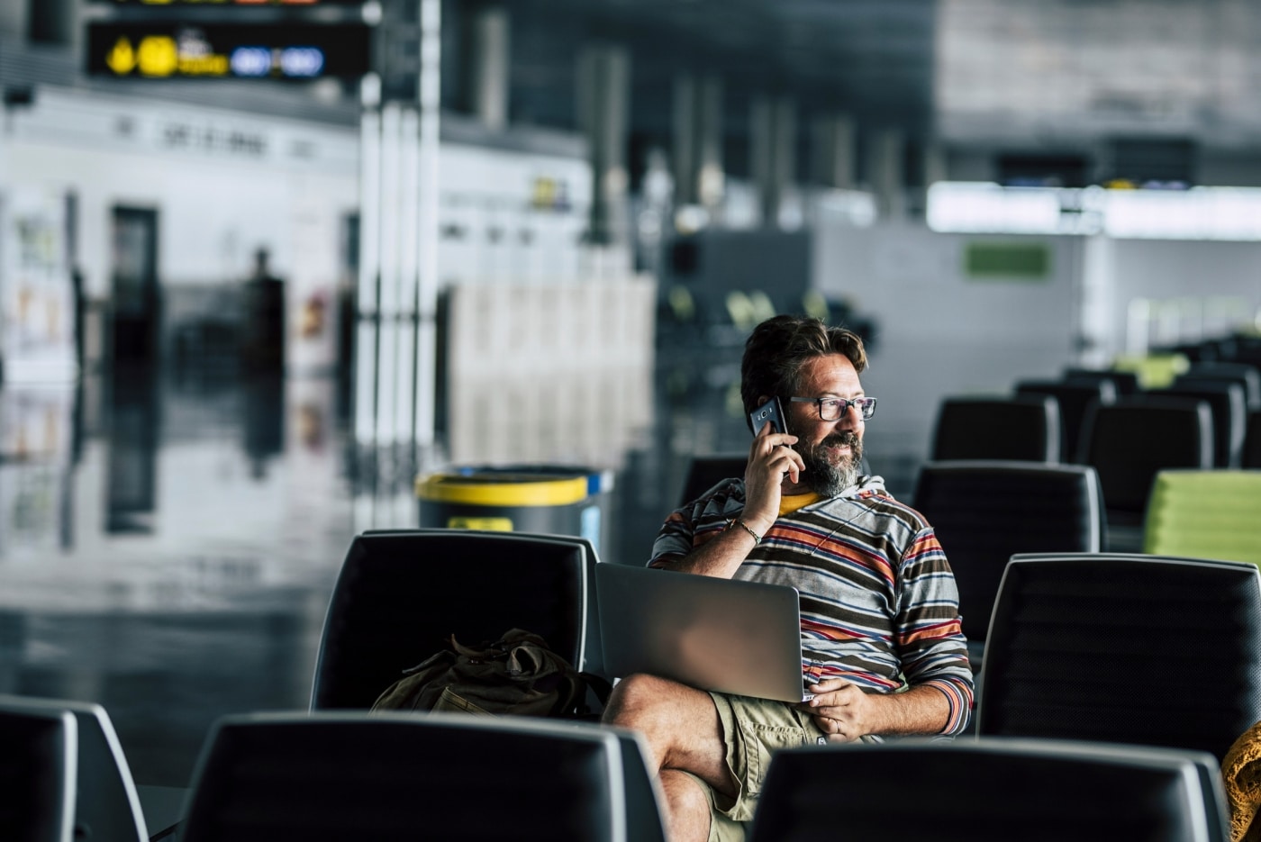 Man on the phone at an airport gate with laptop on lap